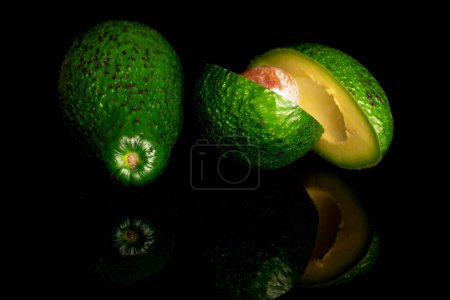 Photo for One whole and two halves, cut across, ripe green avocados, on a black  background. - Royalty Free Image
