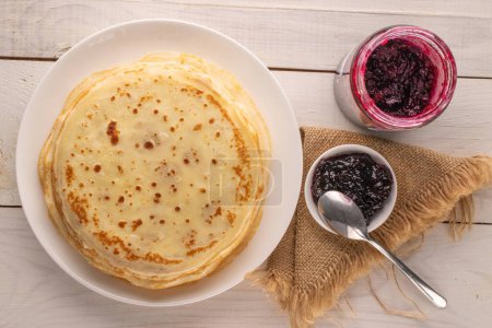 Several sweet pancakes with ceramic plate and jam on wooden table, macro, top view.