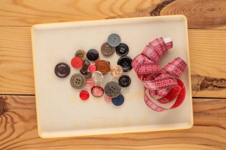Photo for Many buttons in a plastic container and tape measure for seamstresses on a wooden table, macro, top view. - Royalty Free Image