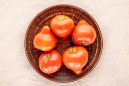 Photo for Several red tomatoes with a clay plate on a linen cloth, macro, top view. - Royalty Free Image