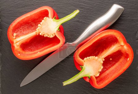 Foto de Dos mitades de pimiento rojo dulce con cuchillo de escoba en piedra de pizarra, macro, vista superior. - Imagen libre de derechos