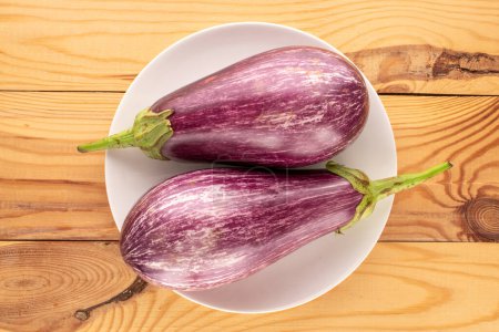 Photo for Two ripe eggplants with white ceramic plate on wooden table, macro, top view. - Royalty Free Image