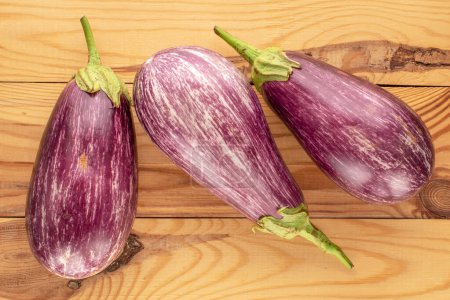 Photo for Three ripe eggplants on a wooden table, macro, top view. - Royalty Free Image