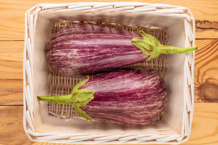 Photo for Two ripe eggplants in a basket on a wooden table, macro, top view. - Royalty Free Image