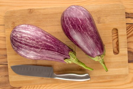 Photo for Two ripe eggplants with bamboo cutting board and knife on wooden table, macro, top view. - Royalty Free Image