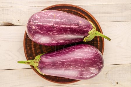 Photo for Two ripe eggplants with a clay plate on a wooden table, macro, top view. - Royalty Free Image