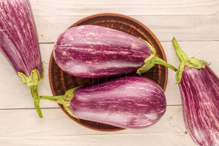 Photo for Four ripe eggplants with a clay plate on a wooden table, macro, top view. - Royalty Free Image