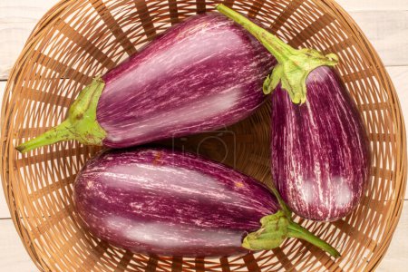 Photo for Three ripe eggplants in a straw dish on a wooden table, macro, top view. - Royalty Free Image
