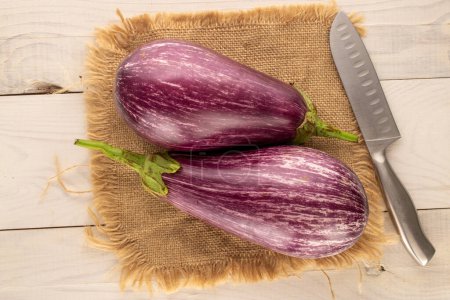 Photo for Two ripe eggplants with jute napkin and knife on wooden table, macro, top view. - Royalty Free Image
