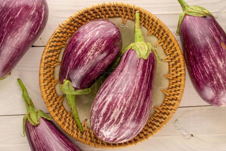 Photo for Several ripe eggplants with a ceramic plate on a wooden table, macro, top view. - Royalty Free Image