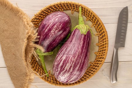 Photo for Two ripe eggplants with ceramic plate and knife on wooden table, macro, top view. - Royalty Free Image
