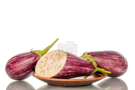 Photo for Two whole and one half juicy eggplant on a clay plate, macro, isolated on white background. - Royalty Free Image