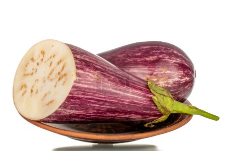 Photo for One whole and one half juicy eggplant on a clay plate, macro, isolated on white background. - Royalty Free Image