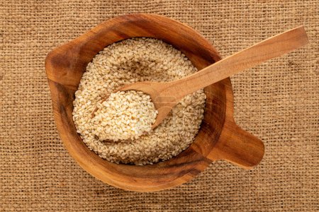 Photo for White sesame seeds with a wooden spoon in a wooden cup on a jute cloth, macro, top view. - Royalty Free Image