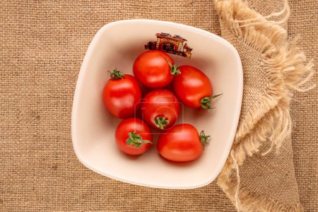 Foto de Varios tomates cóctel en un plato de cerámica sobre un paño de yute, macro, vista superior. - Imagen libre de derechos
