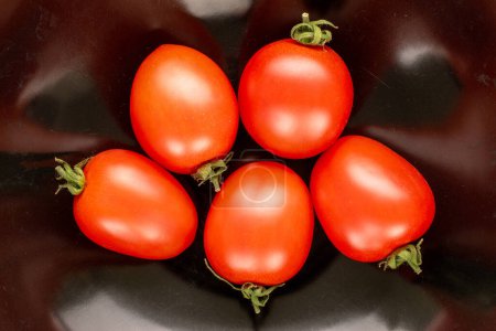 Foto de Varios tomates cóctel en un plato de cerámica negro, macro, vista superior. - Imagen libre de derechos