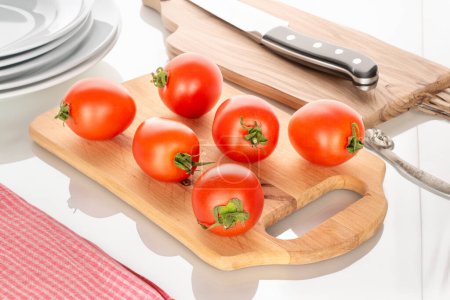 Foto de Varios tomates cherry maduros en una mesa de cocina de madera con utensilios y un cuchillo en la mesa, macro. - Imagen libre de derechos