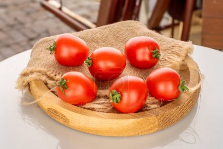 Foto de Varios tomates cherry maduros con una bandeja de madera en la mesa de un café de la calle, macro. - Imagen libre de derechos