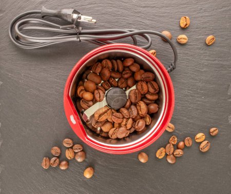 One electric coffee grinder with coffee beans on slate stone, macro, top view.