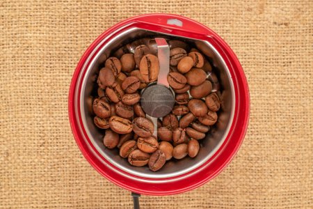 One electric coffee grinder with coffee beans on a jute cloth, macro, top view.