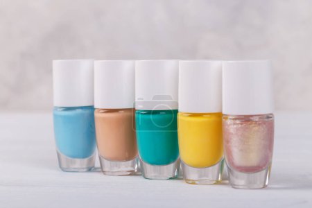 Foto de Esmalte de uñas cinco botellas de colores sobre fondo gris, espacio para copiar - Imagen libre de derechos