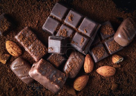 Haufen verschiedener Schokoladenbonbons in Großaufnahme auf einem schwarzen Holztisch im Dunkeln