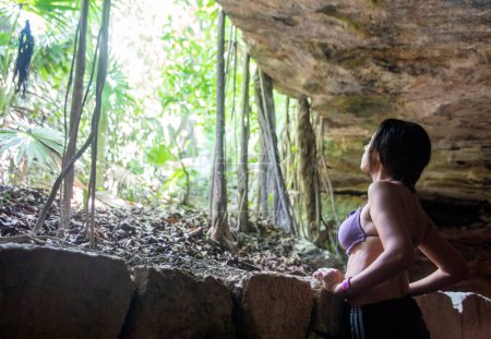Foto de Mujer mirando desde el interior de una cabaña cueva de piedra en el parque Xcaret en la Riviera Maya en México, este es un lugar ideal para ir de vacaciones. - Imagen libre de derechos