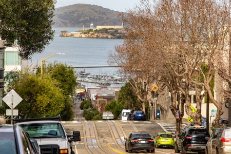 Téléchargez les photos : La célèbre rue Lombard à San Francisco avec le tram et l'île d'Alcatraz en arrière-plan, en Californie, États-Unis. Rue raide avec de nombreuses pentes et collines californiennes. Concept Amérique. - en image libre de droit