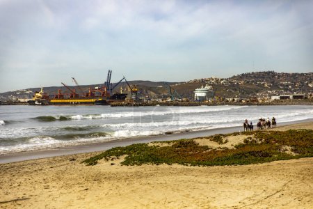 Foto de Una hermosa playa en Ensenada con el puerto en el fondo y gente montando a caballo junto al mar, este es uno de los mejores lugares turísticos de Baja California, México. - Imagen libre de derechos