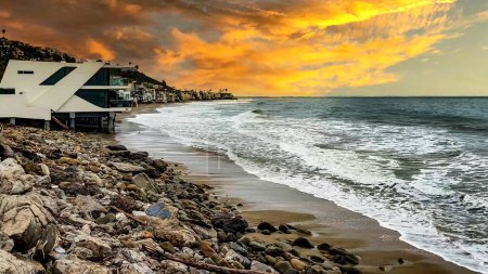 Téléchargez les photos : La falaise et la plage sur l'océan Pacifique de la belle ville californienne de Malibu, près de la célèbre ville de Los Angeles aux États-Unis d'Amérique, sous un ciel orange au coucher du soleil. - en image libre de droit