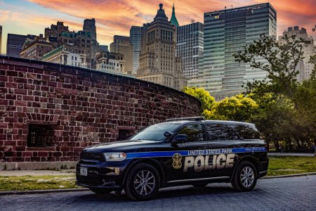 Téléchargez les photos : New York, États-Unis ; 1er juin 2023 : Voiture de patrouille officielle de la police de New York, avec la ligne d'horizon Big Apple et Manhattan en arrière-plan, sous un ciel orange levant. - en image libre de droit