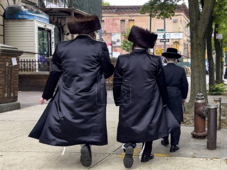 Photo for New York, USA; June 3, 2023: Three Orthodox Jewish men walking through the Williamsburg neighborhood of Brooklyn, where you will witness one of the most striking contrasts in the Big Apple. - Royalty Free Image
