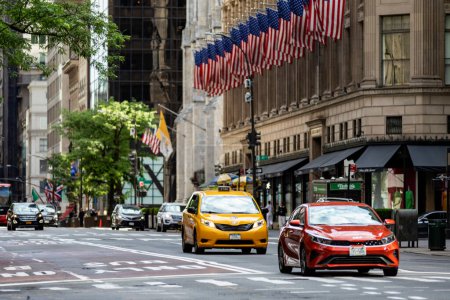 Foto de Nueva York, Estados Unidos; 4 de junio de 2023: taxis y vehículos amarillos circulando a lo largo de la 5ª avenida bajo las típicas banderas estadounidenses de Manhattan, en el corazón de la Gran Manzana en la ciudad de Nueva York (Estados Unidos)). - Imagen libre de derechos