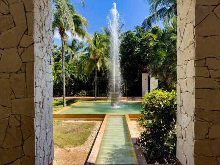 Schöne Fontäne eines Swimmingpools eines Luxushotels in der Karibik, mit einem breiten Wasserstrahl inmitten der tropischen Vegetation dieser idealen Gegend für Sommerurlaub und Entspannung.