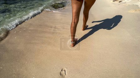 Legs of a sexy young woman enjoying a white sandy beach of the Riviera Maya, with crystal clear turquoise water typical of the Caribbean, as she heads to her resort in Mexico to enjoy her vacation.