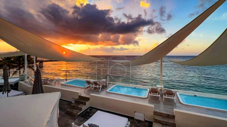 Incroyable coucher de soleil depuis un balcon d'un complexe de luxe dans les Caraïbes, avec un fond de mer turquoise cristalline, hôtel équipé d'un jacuzzi et de piscines privées idéales pour se détendre.