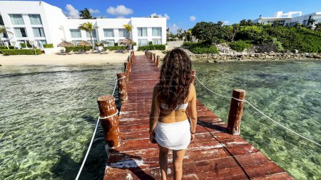 Eine Frau spaziert an der Seebrücke eines paradiesischen Strandes an der Riviera Maya (Mexiko) entlang. Dieses Dock liegt an einem kristallklaren türkisfarbenen Wasser, das zu dem für diesen Ort typischen weißen Sandstrand führt..