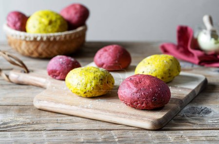 Fresh homemade yellow and pink buns made with seeds, whole flour and natural food colourings as red beetroot and turmeric. Group of rolls on wooden cutting board and table, napkin, turmeric flour