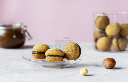 Hazelnut biscuits baci di dama or ladys kisses are traditional Italian dessert made as a sandwich with two cookies and chocolate cream. There are group of cookies on glass plate, jars with chocolate