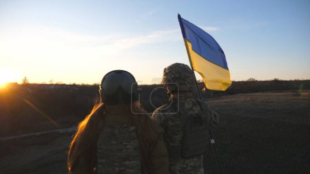Soldiers of ukrainian army raising flag of Ukraine against background of sunset. People in military uniform lifted up yellow-blue flag. Victory against russian aggression. Invasion resistance concept.