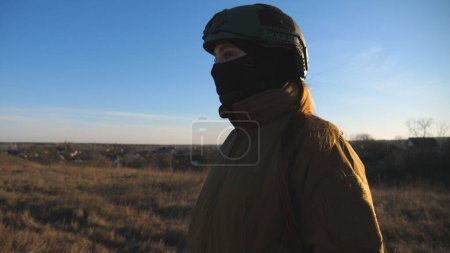 Foto de Soldado del ejército ucraniano caminando en el campo. Mujer con uniforme militar y casco yendo al prado al atardecer. Ucrania victoria contra la agresión rusa. Concepto de resistencia a la invasión. Movimiento lento - Imagen libre de derechos