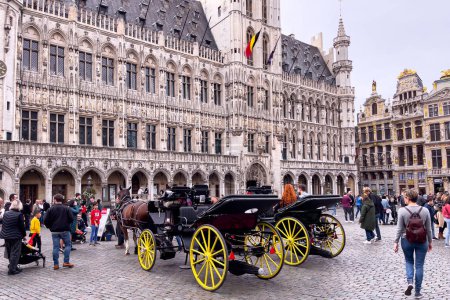 Foto de Turistas caminando cerca de carruajes tirados por caballos en la Grand Place en Bruxelles - Imagen libre de derechos
