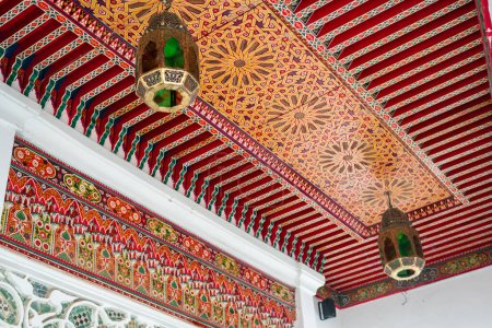 Linterna tradicional colgada en un colorido techo de madera decorado dentro de un antiguo riad en Marruecos