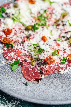 A close-up of a delicious veal carpaccio, seasoned with salt, black pepper, and fresh herbs