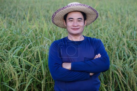 Photo for Handsome Asian man farmer is at paddy field, wears hat, blue shirt, cross arms on chest, feel confident. Concept ,Agriculture occupation. Farmer with organic rice. - Royalty Free Image