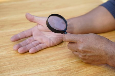 Photo for Closeup hand holds magnifying glass to inspect palm lines. Concept : palmistry, astrology. Foretelling, mystery, magic, fortune, fate. Prediction for future life , events.  Palmist predicting. - Royalty Free Image