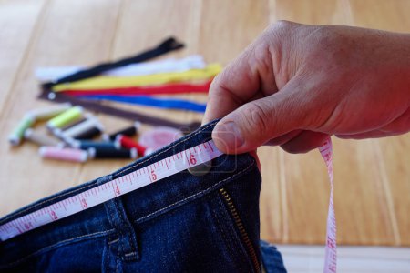 Photo for Closeup tailor hand use measuring tape to measure width of jeans waist. Concept, DIY, sewing. Handcraft. Design ,fix or repair of cutting clothes. - Royalty Free Image