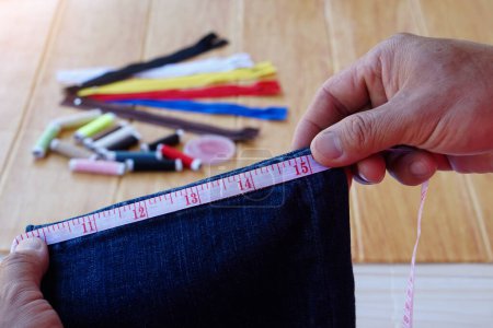 Photo for Closeup hands use measuring tape to measure width of jeans leg. Concept, DIY, sewing. Handcraft. Tailor, Repair clothing at home. Check size. prepare to cut shorten the jeans. - Royalty Free Image