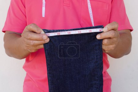 Photo for Closeup tailor uses measuring tape to measure width of jeans leg. Concept, DIY, sewing. Handcraft. Tailor, Repair clothing at home. Check size. prepare to cut shorten the jeans. - Royalty Free Image
