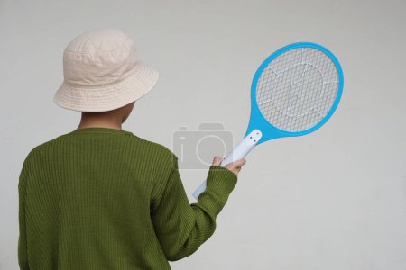 Photo for Back view of boy wears hat, holds mosquito electric swatter racket.   Concept, electric device to kill mosquitoes, insects, bugs by swatting to flying insects - Royalty Free Image